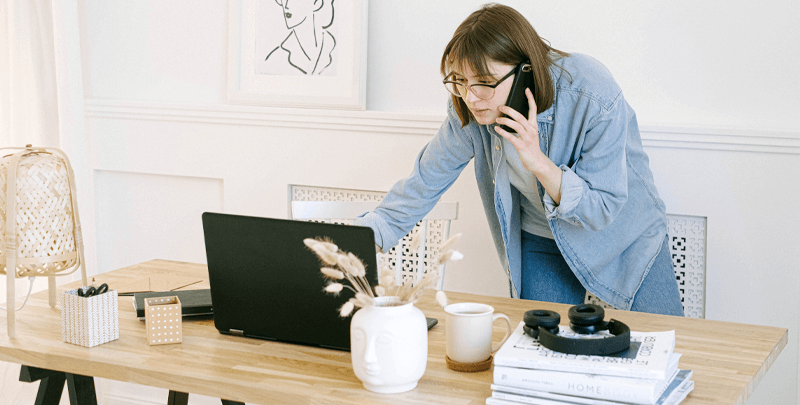 Consultora de negócios usando laptop e telefone em ambiente de escritório, trabalhando com soluções de gestão empresarial e impostos.
