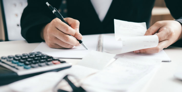 Profissional analisando documentos fiscais e usando calculadora, focado em prestação de serviços de contabilidade, consultoria tributária e assistência fiscal para empresas.