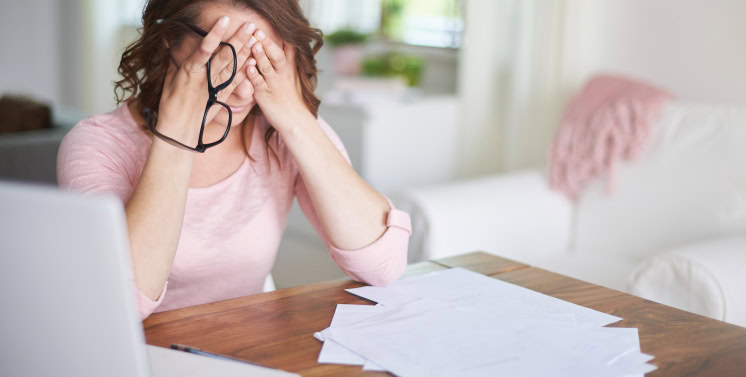 Estresse com documentos fiscais e impostos, mulher cansada com papéis e laptop em ambiente de home office, ansiedade financeira, dificuldade na gestão tributária, solução em impostos e consultoria fiscal.