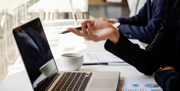 Profissional usando laptop e smartphone em ambiente de escritório, com gráficos e documentos ao redor, representando serviços de consultoria tributária e soluções fiscais do Dootax.