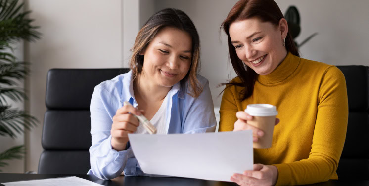 1. Duas mulheres sorrindo enquanto analisam documentos financeiros, representando serviços de consultoria tributária e gestão de impostos com Dootax.