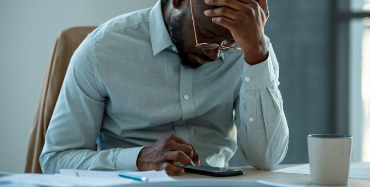 Frustrado com problemas fiscais, homem usando computador e telefone em ambiente de escritório, representando dificuldades na gestão tributária e contábil, tema importante para soluções fiscais e contáveis na Dootax.