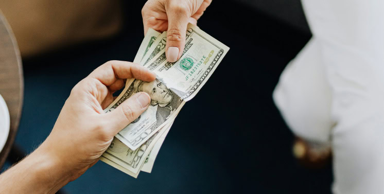 Dinheiro em notas de dólar sendo trocado entre duas pessoas, símbolo de transações financeiras, pagamento e negócios, reforçando temas de economia, serviços fiscais e consultoria tributária com Dootax.