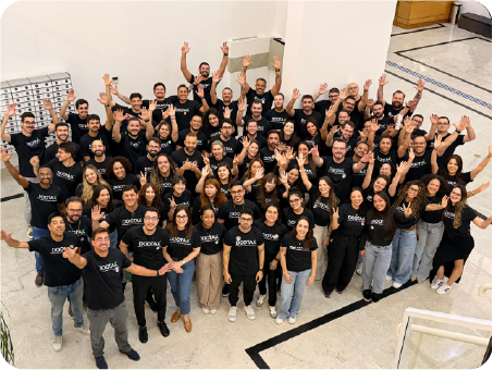 Equipe de colaboradores da Dootax reunida em ambiente interno, todos usando camisetas pretas com o logo da empresa, celebrando e sorrindo para a câmera, demonstrando união e entusiasmo.
